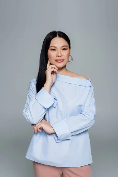 Stylish asian woman touching face and looking at camera isolated on grey — Stock Photo