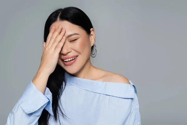 Eccitato asiatico donna in camicetta copertura faccia isolato su grigio — Foto stock