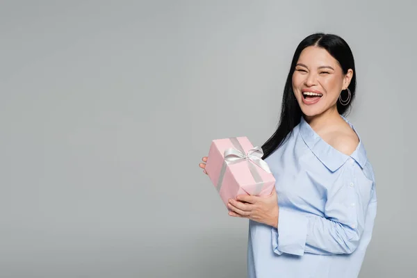 Радостная азиатка держит присутствующую изолированную на сером — стоковое фото