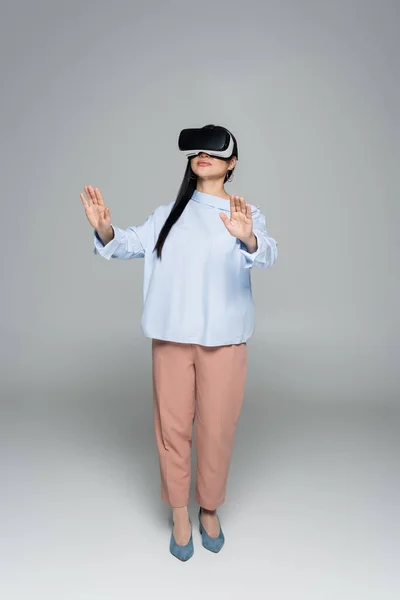 Full length of stylish woman in virtual reality headset on grey background — Stock Photo
