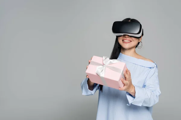 Smiling woman in vr headset holding gift isolated on grey — Stock Photo