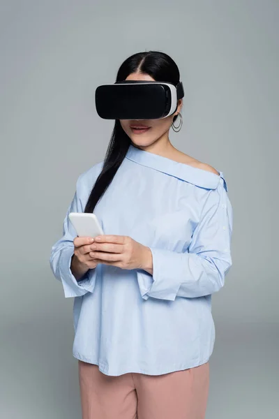 Mujer con estilo en auriculares vr utilizando el teléfono celular aislado en gris - foto de stock