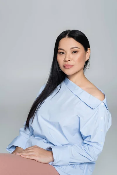 Trendy asian woman in blouse with naked shoulder looking at camera isolated on grey — Stock Photo