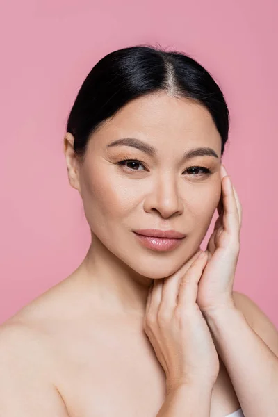 Femme asiatique avec des épaules nues touchant le visage isolé sur rose — Photo de stock