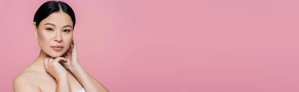 Asian woman with naked shoulder looking at camera isolated on pink with copy space, banner — Stock Photo