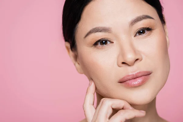 Portrait of brunette asian woman with makeup looking at camera isolated on pink — Stock Photo