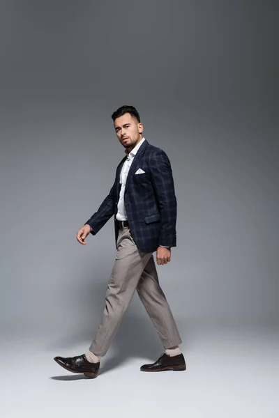In voller Länge junger bärtiger Geschäftsmann im Anzug, der auf grau läuft — Stockfoto
