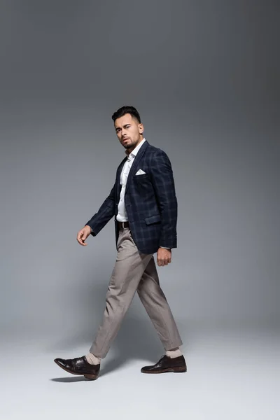 Full length of young bearded businessman in suit walking on grey — Stock Photo