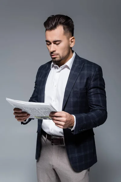 Joven hombre de negocios barbudo en chaqueta a cuadros leyendo periódico aislado en gris - foto de stock