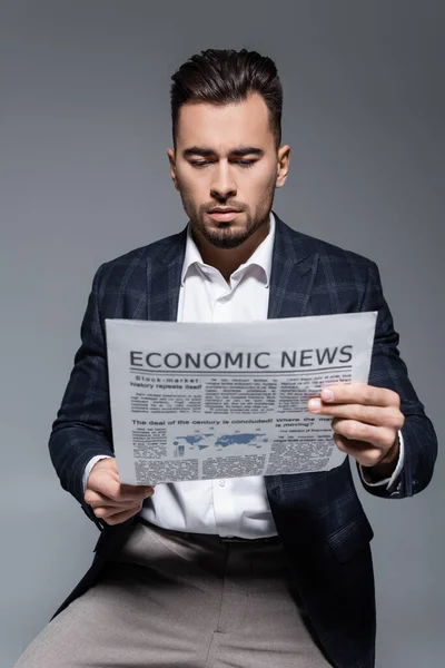 Hombre de negocios barbudo en chaqueta a cuadros leyendo periódico con noticias económicas aisladas en gris - foto de stock