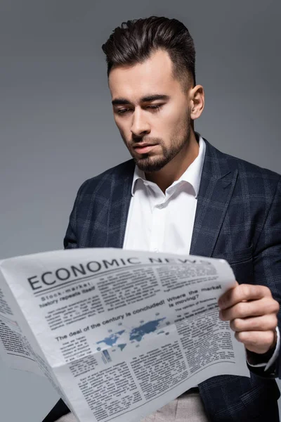 Homme d'affaires barbu en plaid blazer lecture journal avec des nouvelles économiques isolé sur gris — Photo de stock