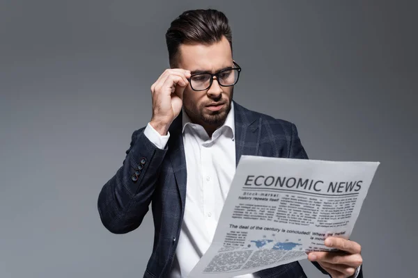 Bearded businessman in plaid blazer and glasses reading newspaper with economic news isolated on grey — Stock Photo