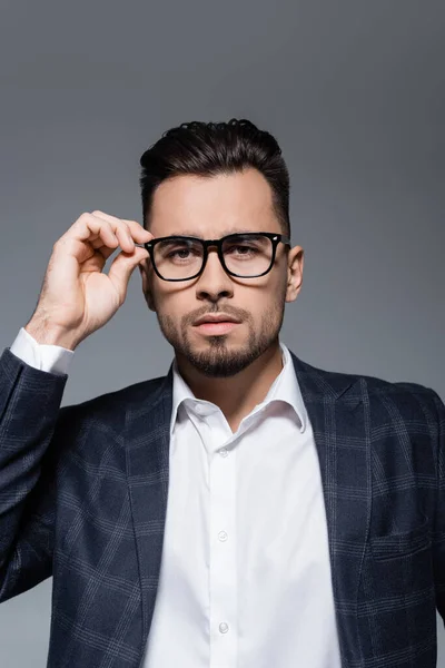 Bearded businessman in blazer adjusting glasses isolated on grey — Stock Photo