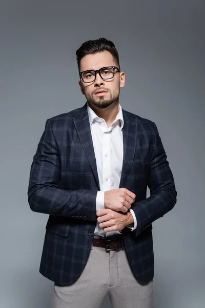 Hombre de negocios barbudo en chaqueta y gafas mirando a la cámara aislada en gris - foto de stock