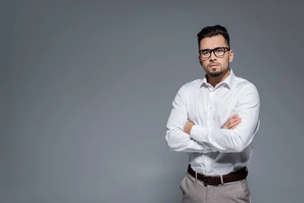 Hombre de negocios barbudo con camisa blanca y gafas de pie con brazos cruzados aislados en gris - foto de stock