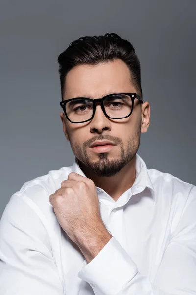 Hombre de negocios barbudo con camisa blanca y gafas mirando a la cámara aislada en gris - foto de stock