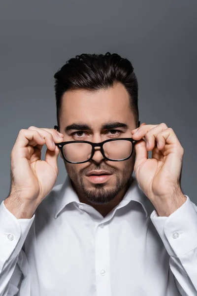 Hombre de negocios barbudo en camisa blanca ajustando gafas aisladas en gris - foto de stock