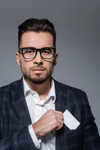 Hombre de negocios en gafas y chaqueta a cuadros poniendo tarjeta en blanco en el bolsillo aislado en gris - foto de stock