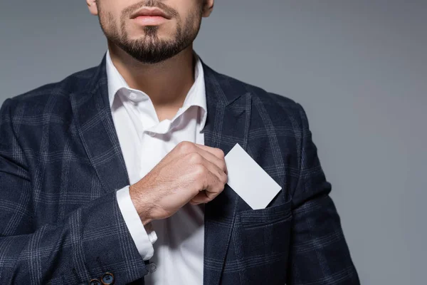 Vista recortada de hombre de negocios en chaqueta a cuadros poner la tarjeta en blanco en el bolsillo aislado en gris - foto de stock