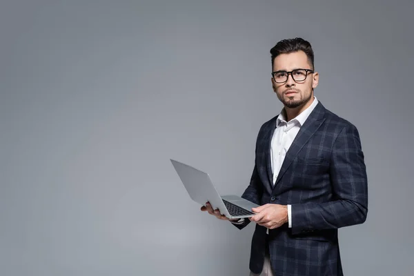 Businessman in suit and glasses holding laptop isolated on grey — Stock Photo
