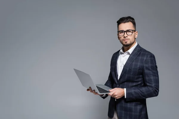 Hombre de negocios con traje y gafas con portátil aislado en gris - foto de stock