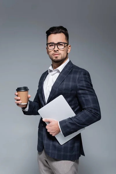 Uomo d'affari in tuta e occhiali con laptop e tazza di carta isolati su grigio — Foto stock