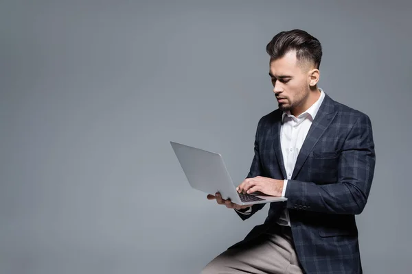 Homem de negócios barbudo em terno usando laptop isolado em cinza — Fotografia de Stock