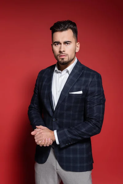 Bearded businessman in checkered blazer with clenched hands on red — Stock Photo