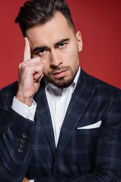 Hombre de negocios barbudo en traje con chaqueta a cuadros mirando a la cámara en rojo — Stock Photo