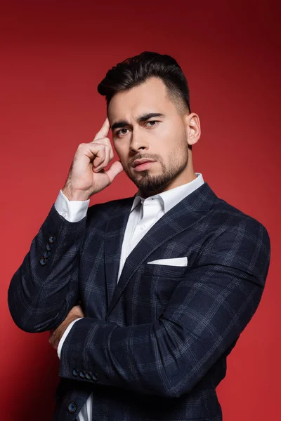 Hombre de negocios barbudo en chaqueta a cuadros mirando a la cámara en rojo — Stock Photo