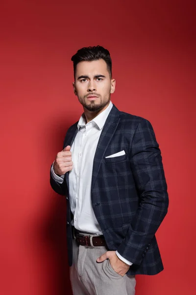 Bearded businessman in suit with checkered blazer standing with hand in pocket on red — Stock Photo