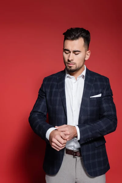 Bearded businessman in checkered blazer adjusting sleeve of white shirt on red — Stock Photo