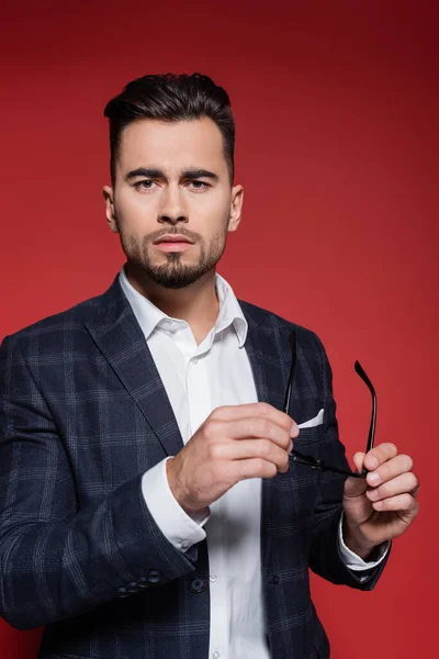 Young businessman in checkered blazer holding glasses on red — Stock Photo