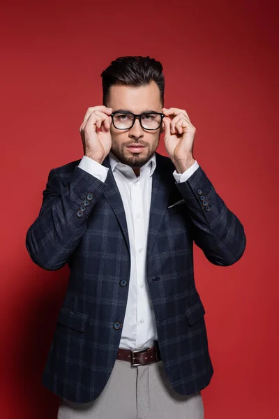 Молодий бізнесмен в плетеному блістері регулює окуляри на червоному — стокове фото
