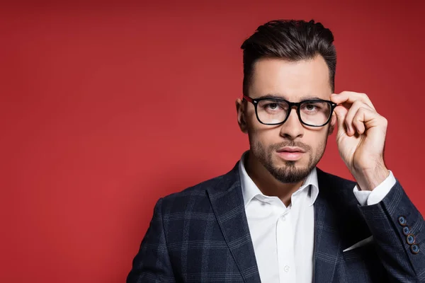 Bearded businessman in plaid blazer adjusting glasses on red — Stock Photo