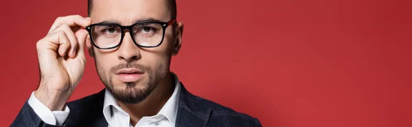 Homme d'affaires barbu en plaid blazer réglage des lunettes sur rouge, bannière — Photo de stock