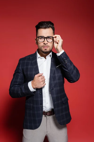 Bearded businessman in plaid suit adjusting glasses on red — Stock Photo