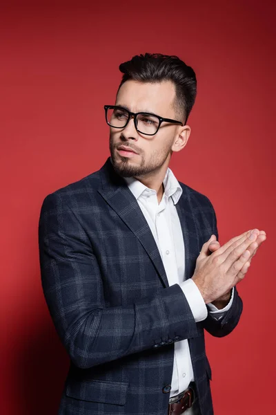 Bearded businessman in checkered suit and glasses looking away on red — Stock Photo