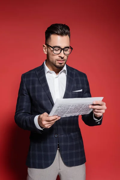 Hombre de negocios barbudo en traje a cuadros y gafas leyendo periódico en rojo - foto de stock