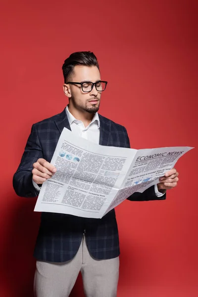 Hombre de negocios barbudo en chaqueta a cuadros y gafas leyendo periódico en rojo - foto de stock