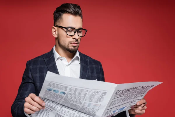 Homme d'affaires barbu en blazer et lunettes lecture journal sur rouge — Photo de stock