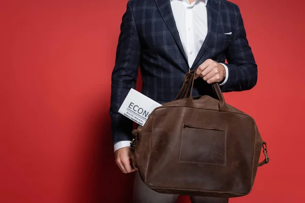 Cropped view of businessman in blazer holding leather bag with newspaper on red — Stock Photo