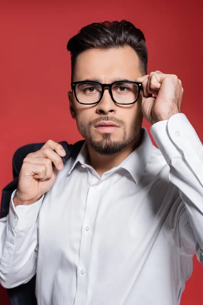 Бородатий бізнесмен у білій сорочці, що регулює окуляри і тримає блістер на червоному — стокове фото