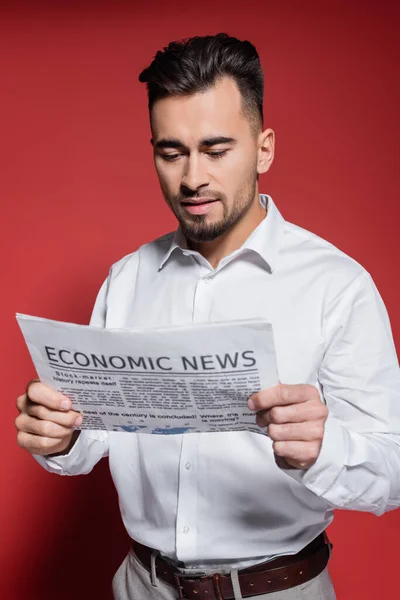 Bearded businessman in white shirt reading economic news on red — Stock Photo