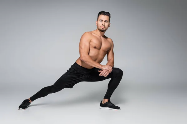 Full length of bearded and muscular sportsman stretching on grey — Stock Photo