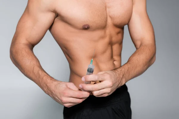 Обрезанный вид безрубашечного и мускулистого спортсмена, держащего шприц со стероидами, изолированными на сером — стоковое фото