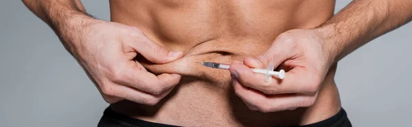 Vue recadrée d'un sportif torse nu s'injectant dans le ventre isolé sur une bannière grise — Photo de stock
