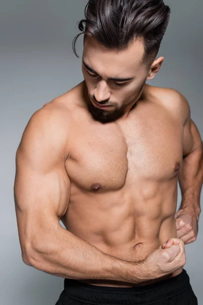 Bearded and muscular sportsman looking muscles isolated on grey — Stock Photo