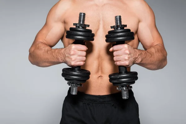 Visão parcial de desportista sem camisa e muscular trabalhando com halteres isolados em cinza — Fotografia de Stock