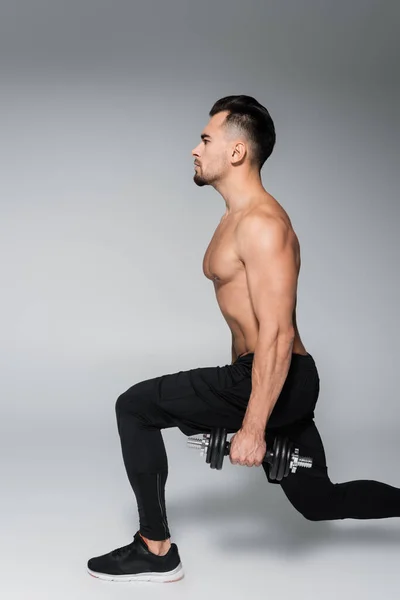 Side view of muscular sportsman working out with dumbbells on grey — Stock Photo